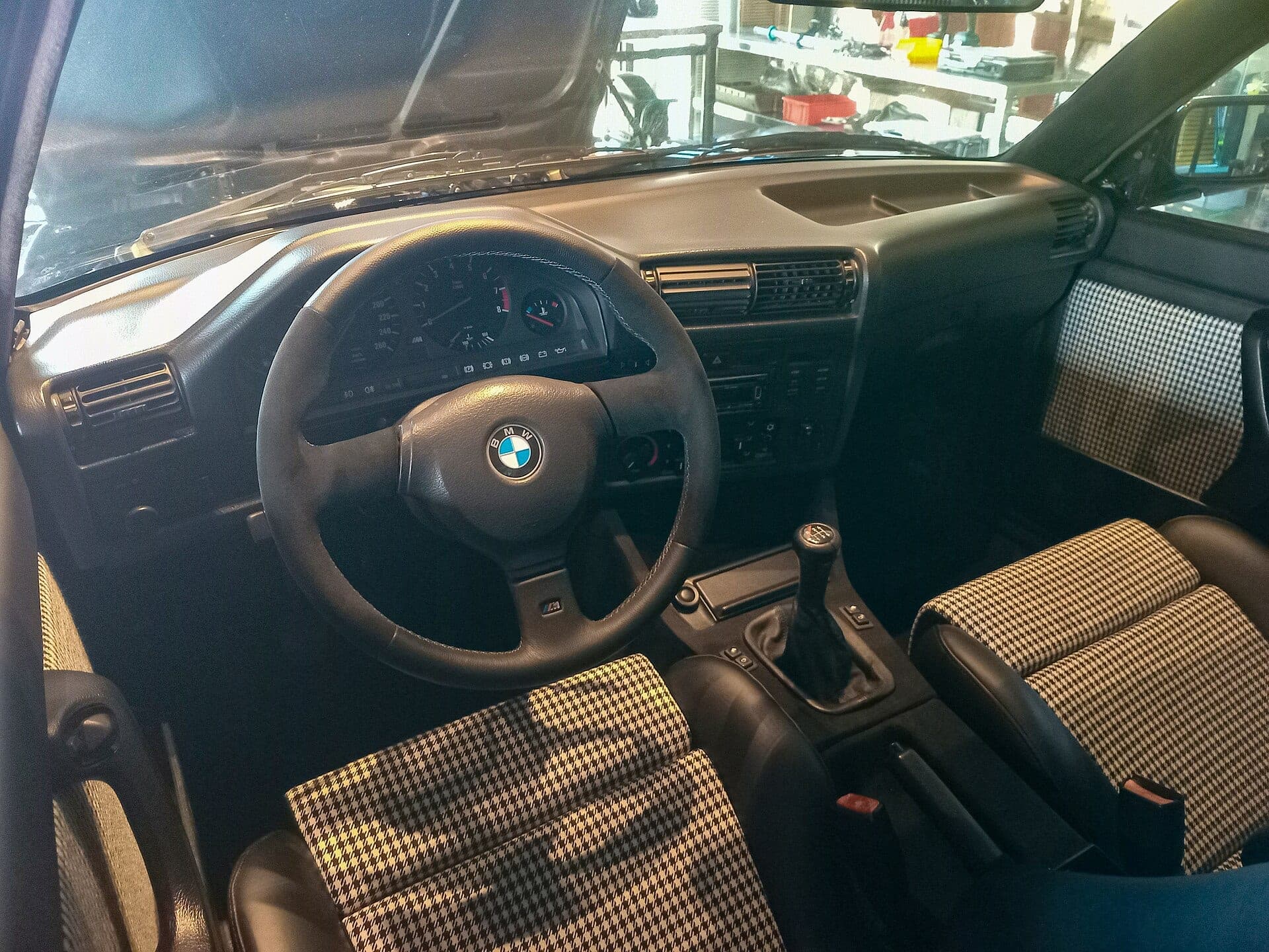 Interior de un BMW M3 E30 con tapicería de pata de gallo, volante M de tres radios y palanca de cinco marchas