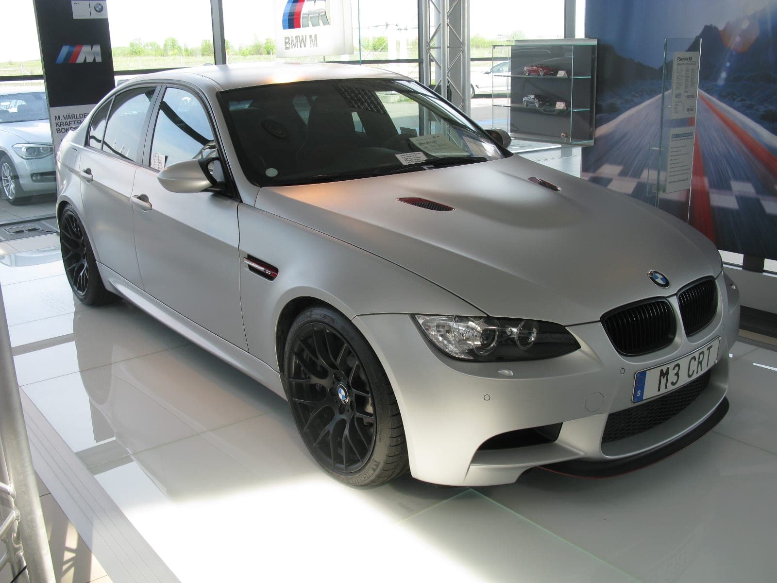 BMW M3 CRT, berlina E90 en gris mate con capó de carbono y filetes rojos, vista de tres cuartos delantera