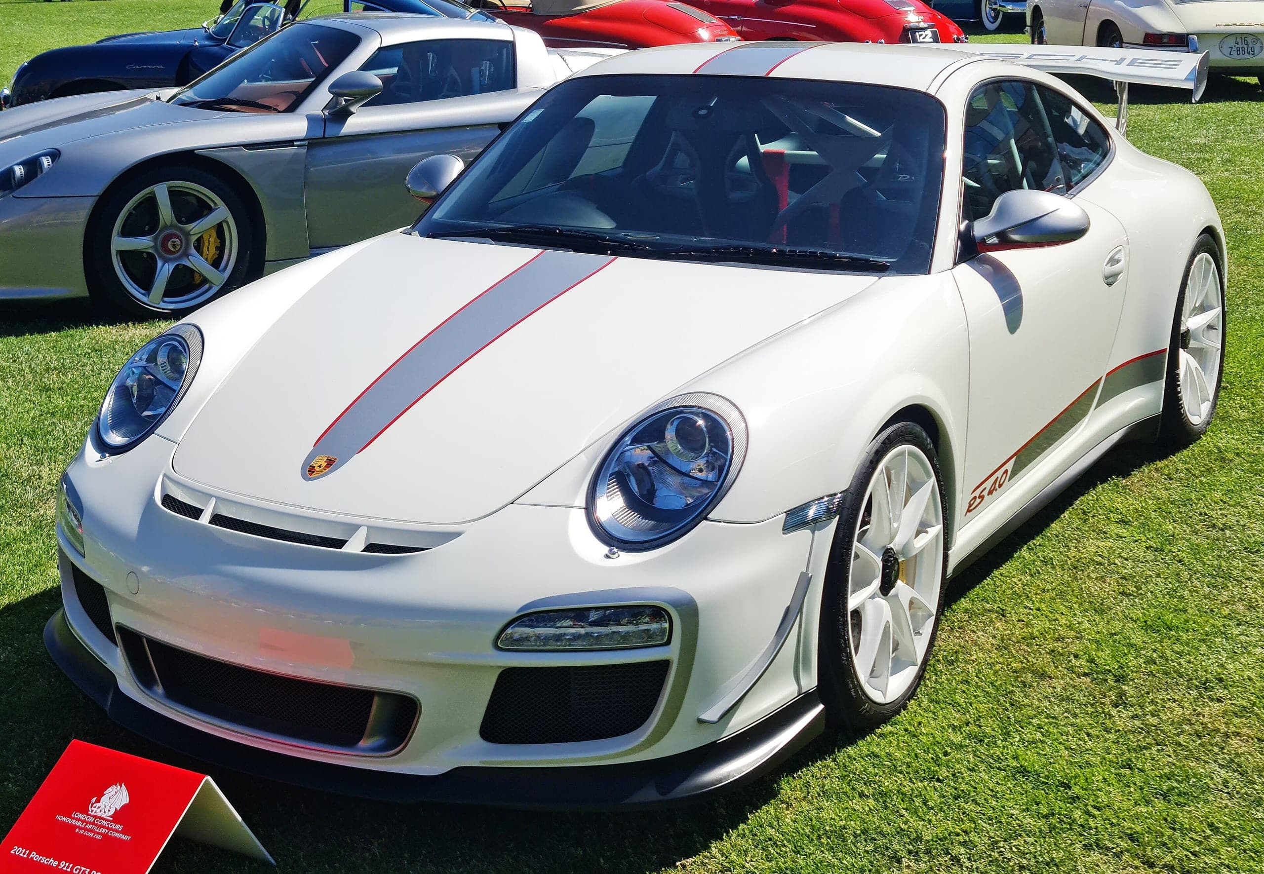 Porsche 911 997 GT3 RS 4.0 blanco con franja central roja y plata, alerones delanteros y el rótulo RS 4.0 en el costado, vista de tres cuartos delantera
