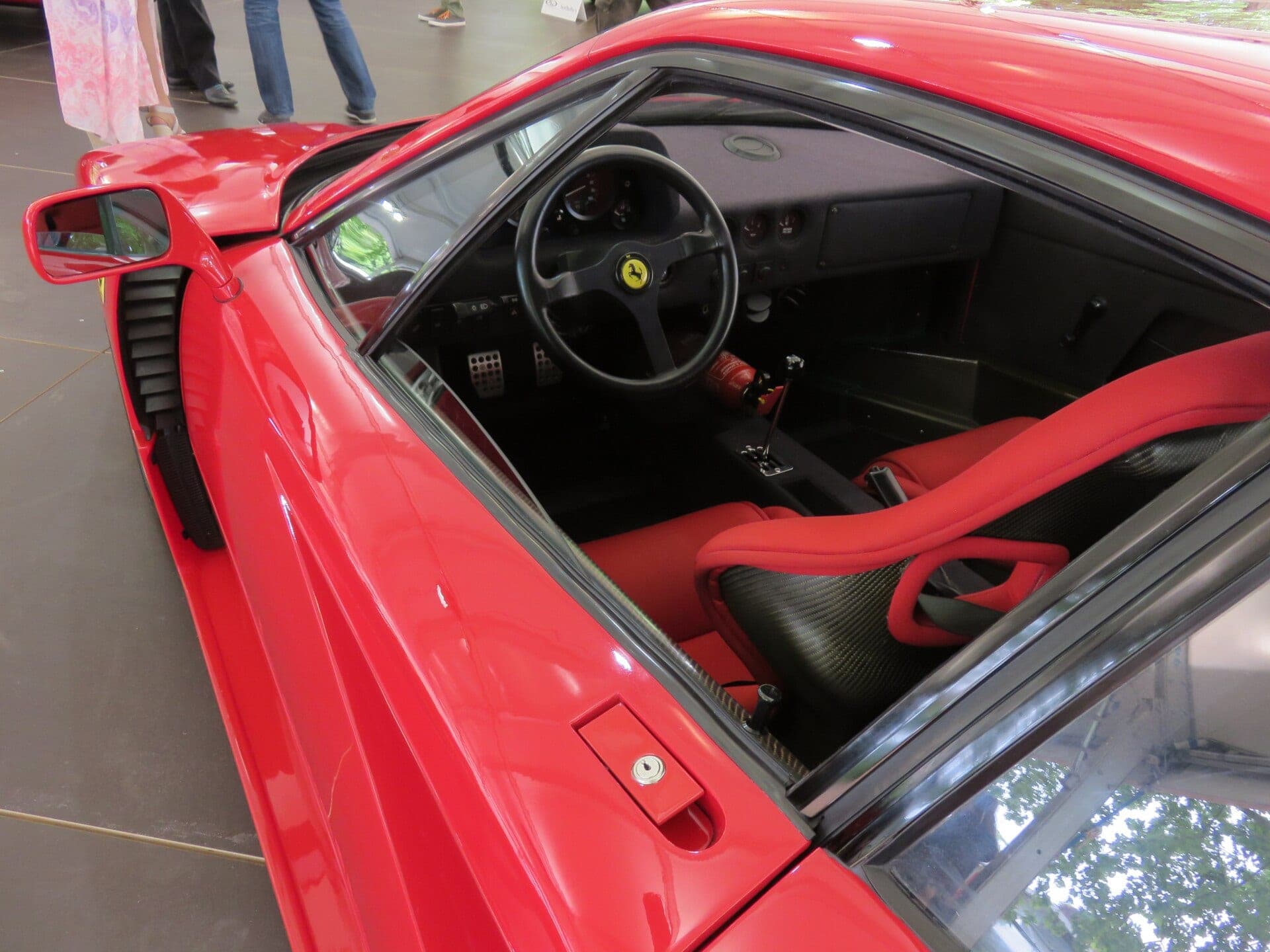 Habitáculo de un Ferrari F40 visto por encima de la puerta abierta, con el volante, la palanca de guía metálica y los asientos de tela roja