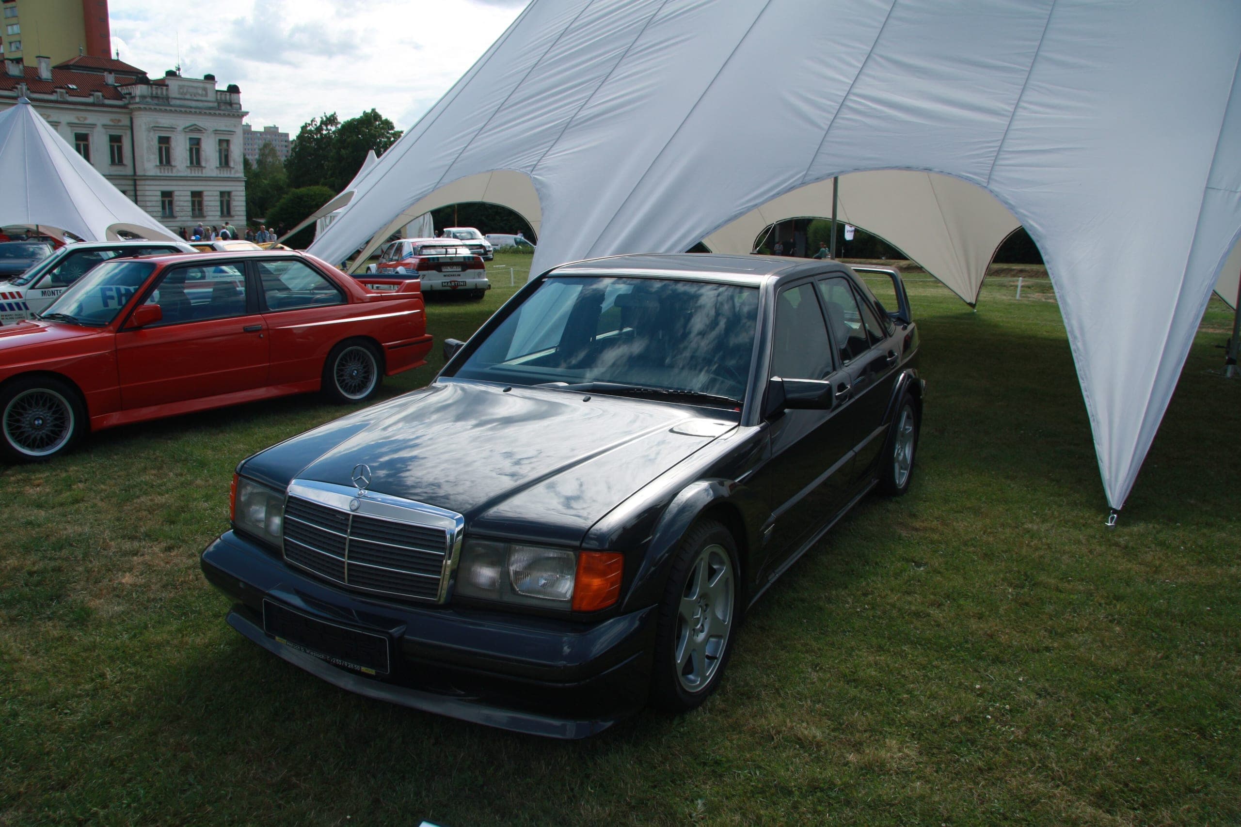 Mercedes-Benz 190E 2.5-16 Evolution II negro sobre hierba en una concentración, con el alerón trasero de dos planos